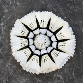 A top-down view of neatly arranged shuttlecocks creating a floral pattern on a dark surface.
