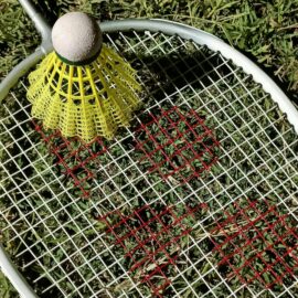 Close-up of a badminton shuttlecock on a racket on grass, highlighting sports equipment.